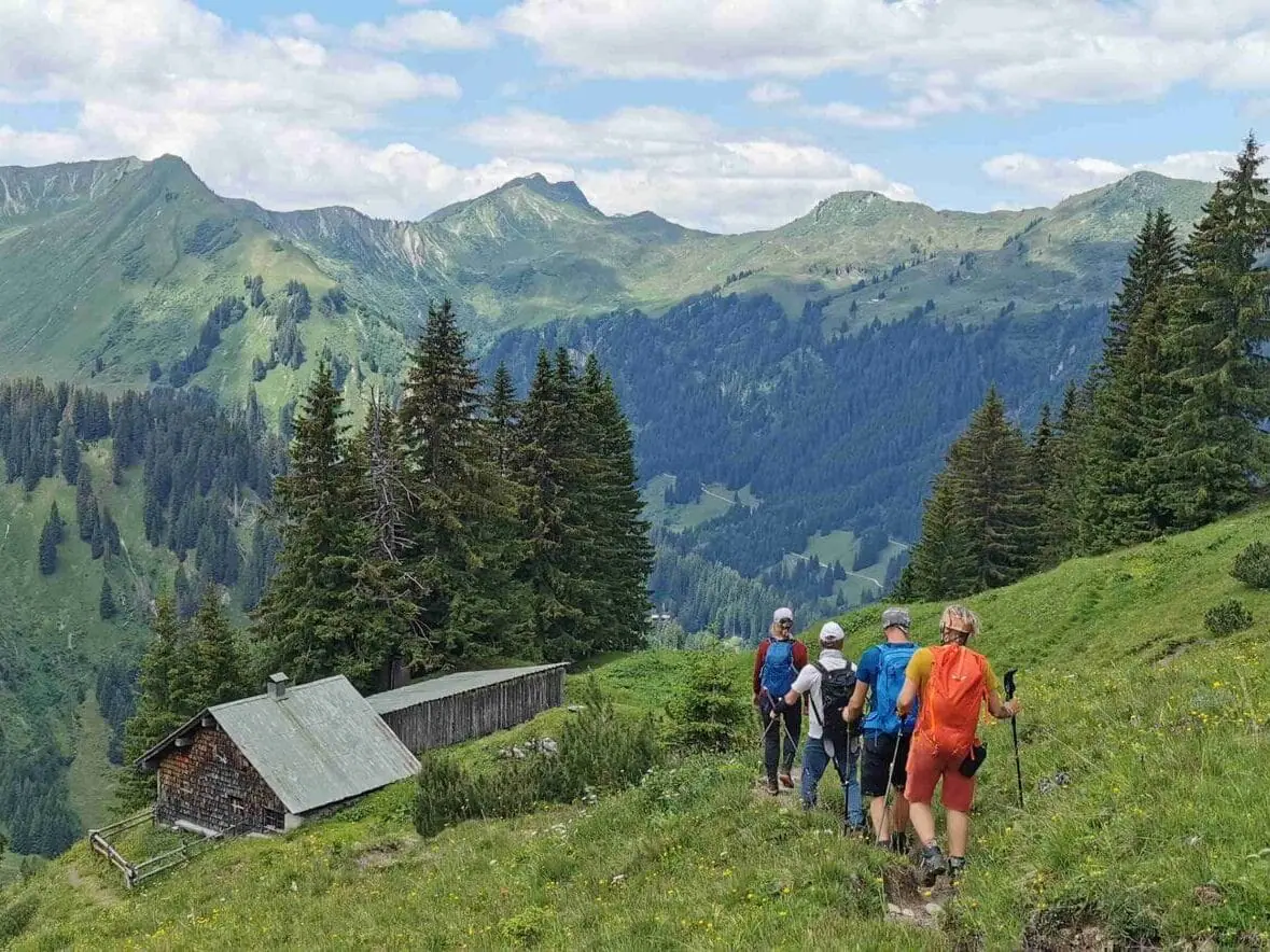 Vier Wanderer auf einem Grasfeld, im Hintergrund die Berge des Kleinwalstertal