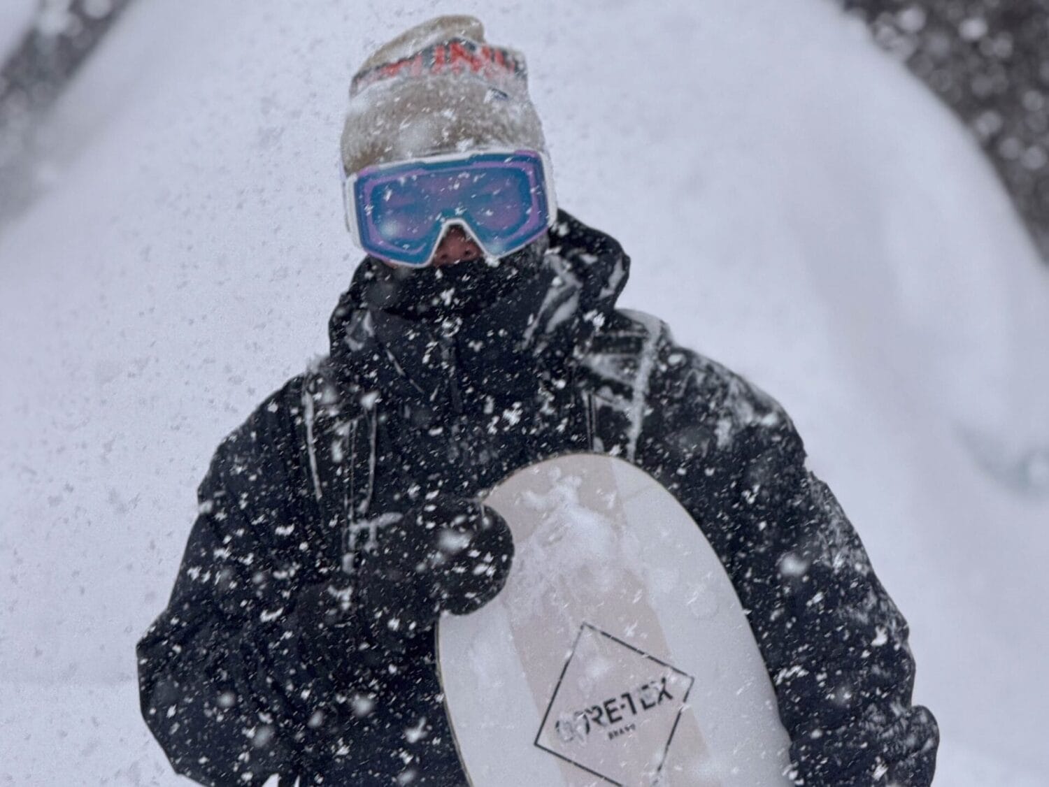 Mann im Schneegestöber mit Snowboard in der Hand schaut in die Kamera