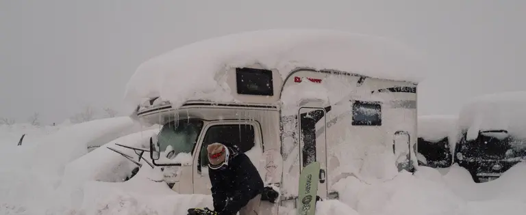 Eingeschneiter Camper und Snowboarder davor