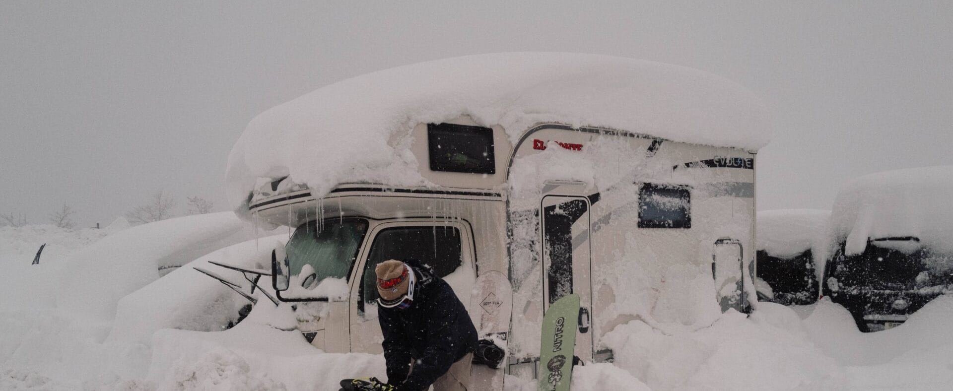 Eingeschneiter Camper und Snowboarder davor