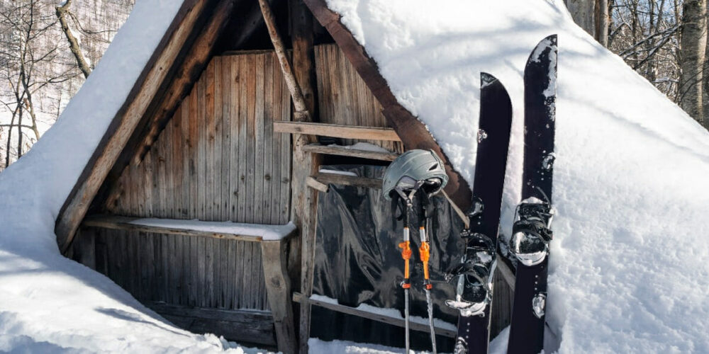 Splitboard Stöcke und Helm im Schnee vor einer Holzhütte